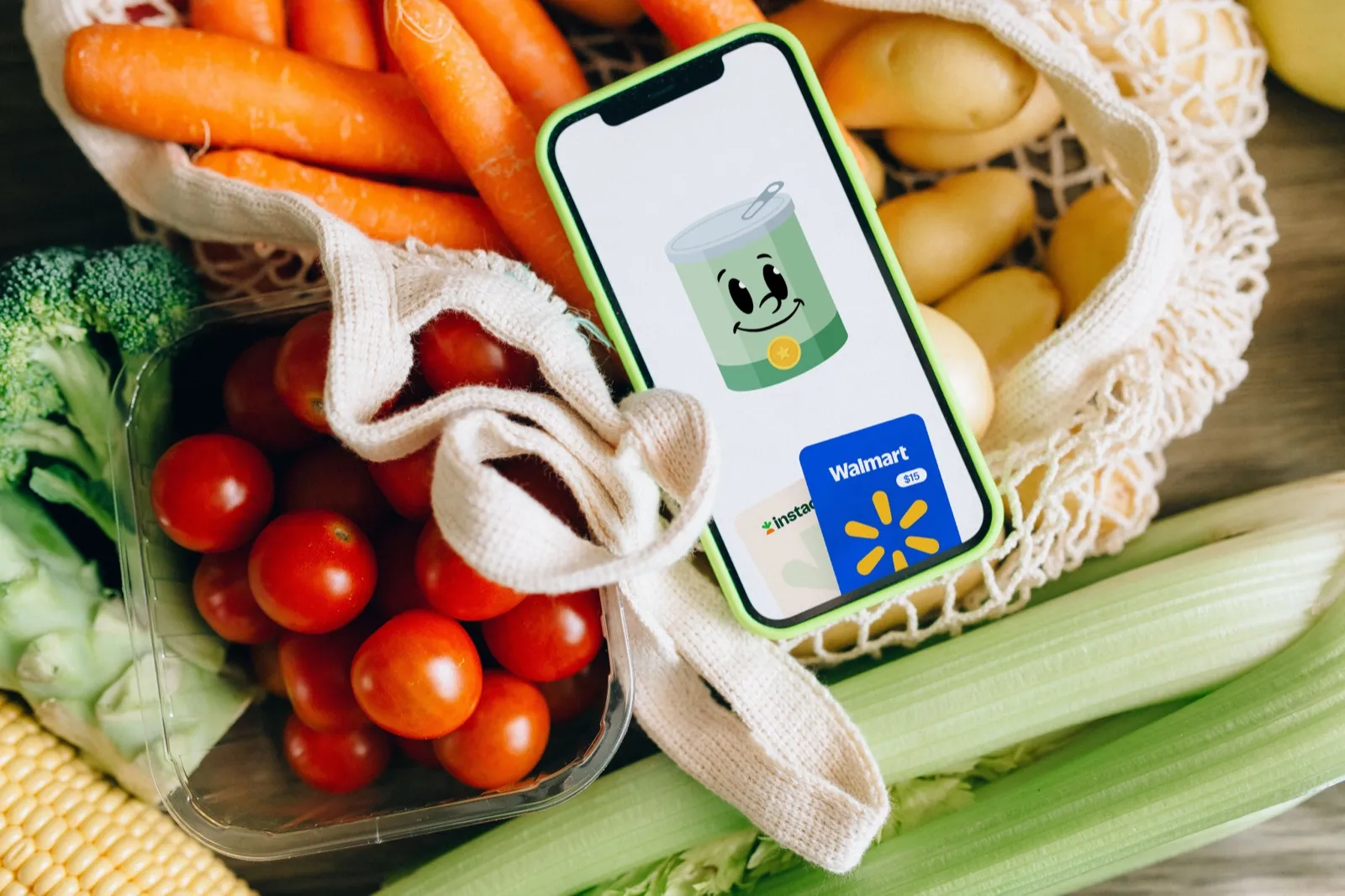A phone showing the Pantry Point app in a grocery bag of carrots and tomatoes